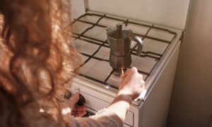Cocina doméstica con placa de gas apagada y una persona abriendo la ventana ante una posible fuga