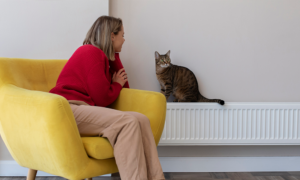 Radiador doméstico con una mano comprobando la temperatura y una llave de purga visible en un salón de vivienda